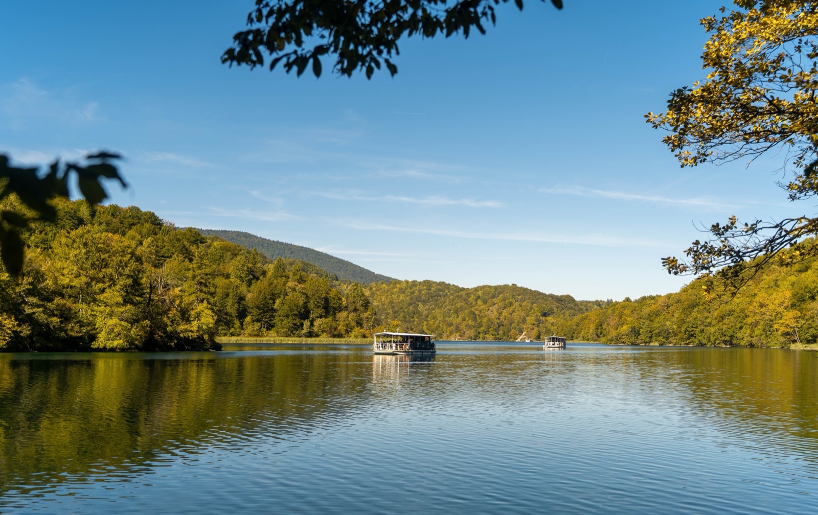 Due battelli elettrici su un lago calmo tra colline boscose sotto un cielo azzurro e limpido